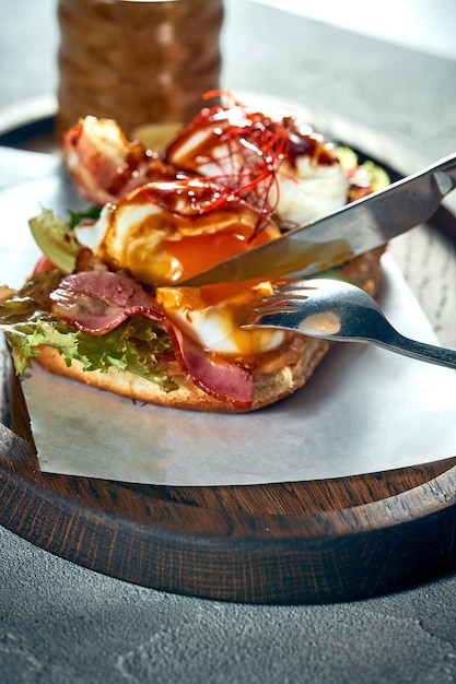 朝食用にトマトベーコンとポーチドエッグのサンドイッチを切る女の子 コンクリートの背景 ハードライト
