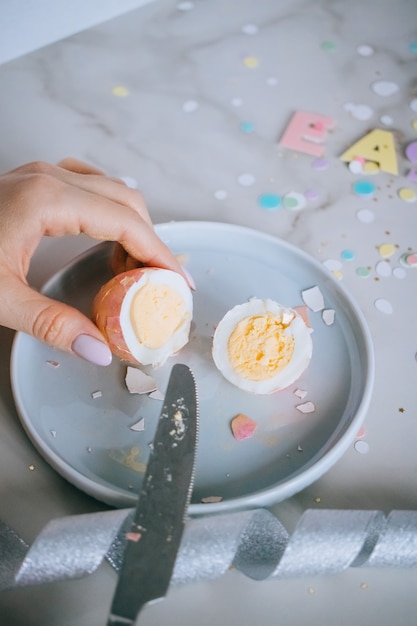Девушка резка золотые пасхальные яйца на фоне мрамора, конфетти, блестки, ленты.