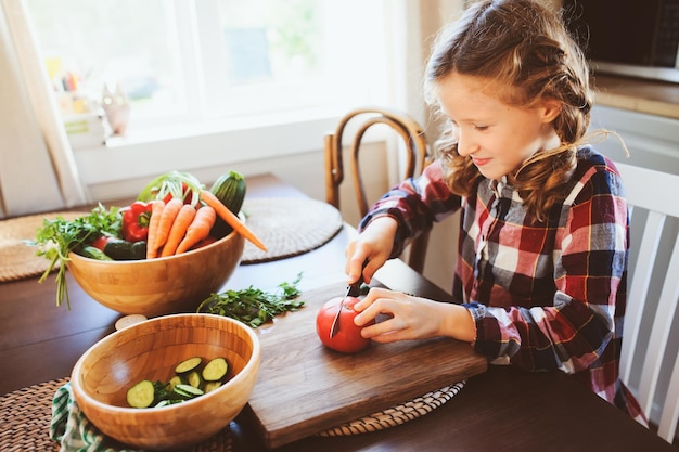 girl cutting tomato on table in kitchen at home