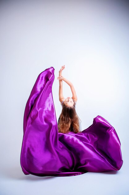 Девушка-танцовщица танцует в фиолетовой ткани. Красивые хореографические элементы в летящем платье.