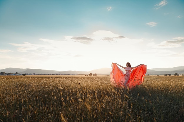 Girl dancing in a field in a beautiful pink dress at sunset