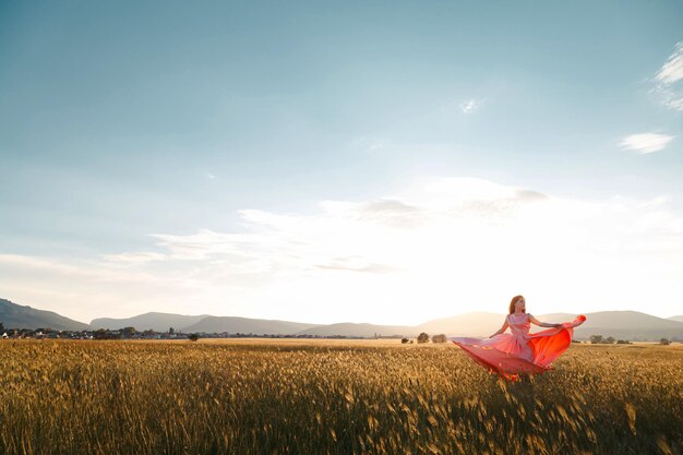 Girl dancing in a field in a beautiful pink dress at sunset