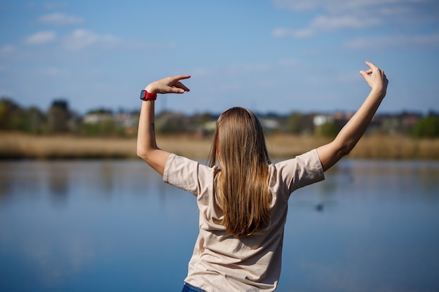 Ragazza che balla vicino al lago, tempo soleggiato. una giovane donna gioisce nella vita, balla e canta. ha un buon umore e un sorriso sul viso.