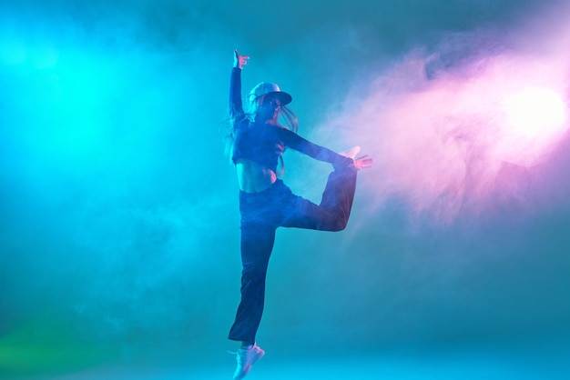 A girl in dark clothes dances on a neon background in smoke modern dance