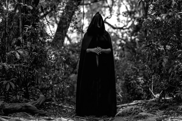 A girl in a dark robe with a knife. It stands in the forest. Happy Halloween.