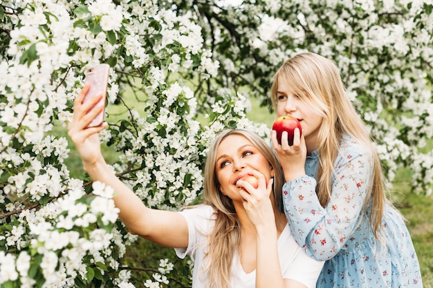 Foto ragazza, figlia con la madre, meli in fiore, alberi, fiori, rami, primavera, estate, bellezza, natura, comunicazione, famiglia, bacio, incontro, lettura di un libro, conversazione