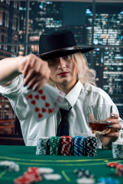 Девушка-дилер или крупье тасует покерные карты в казино на фоне стола с фишками