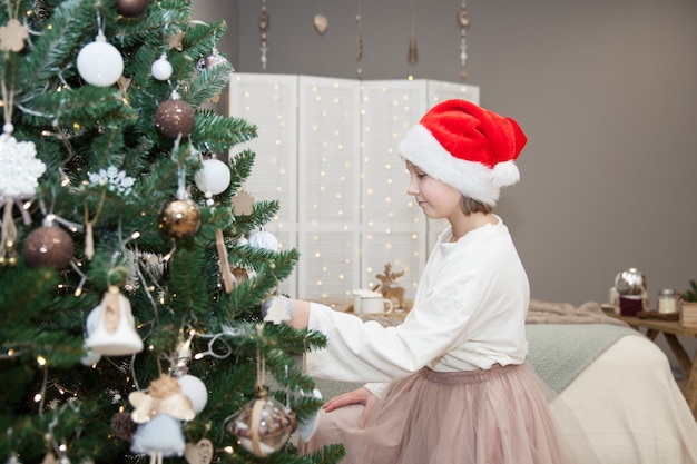 A girl decorates a Christmas tree in a festive bedroom