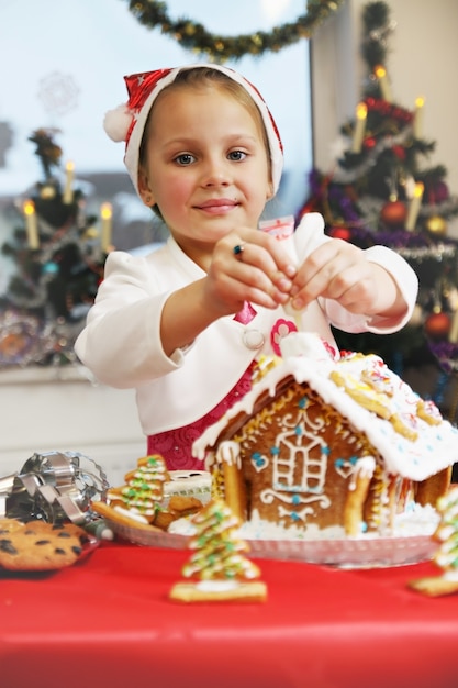 Girl decorates gingerbread house with icing from a tube