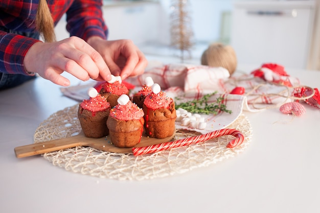 La ragazza decora i bigné di celebrazione di nuovo anno, muffin al cioccolato sul tavolo