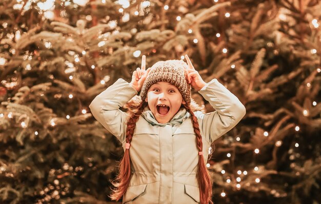 Girl and decorating Christmas tree with ornaments outside. Happy kid is enjoying holidays. Little girl at winter market on town street. Cozy fair and New Year in Poland