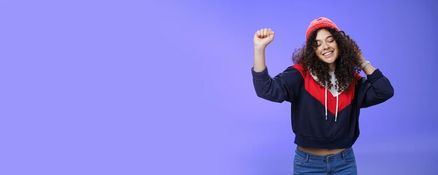 Girl delighted and carefree dancing over blue background with closed eyes and tender smile moving ra