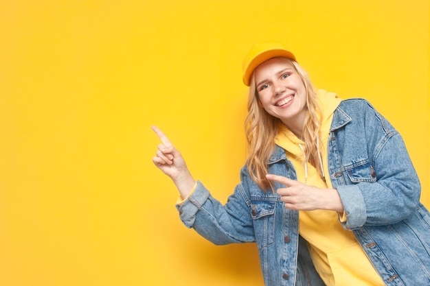 Girl in denim jacket and cap shows with her hand on copy space