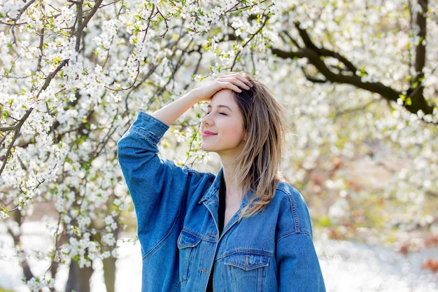 デニムジャケットを着た女の子が公園の開花木の近くに滞在します。春の季節