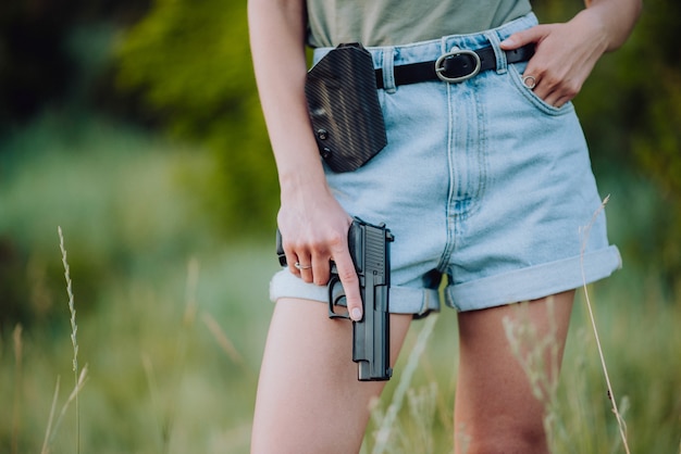 デニムのショートパンツを着て、銃を手にフィールドでポーズをとっている女の子。