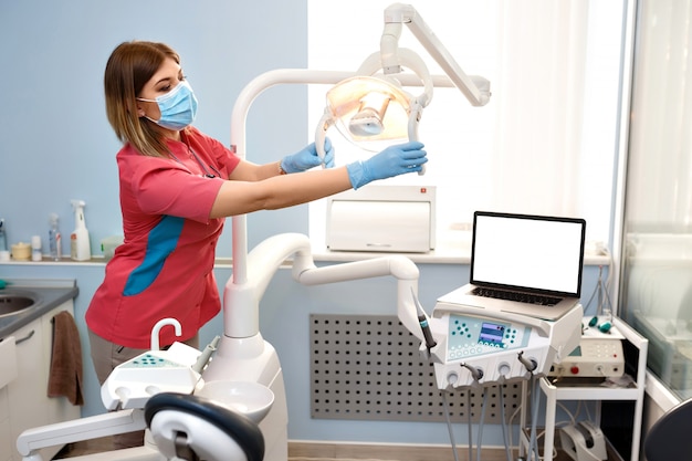 Girl dentist prepares the equipment for operation. On the table is a laptop with empty blank