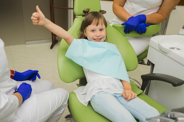 Foto ragazza al dentista che sorride e che dà i pollici in su