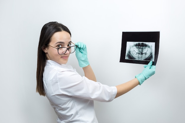 Girl dentist in a white coat holds a snapshot of the patient's teeth.