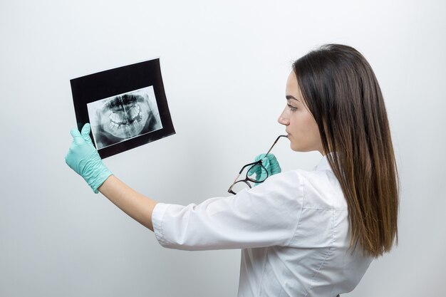 Girl dentist in a white coat holds a snapshot of the patient's teeth.