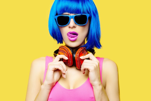 Girl dj in wig sunglasses and pink bathing suit listening music in headphones on yellow background. High quality photo