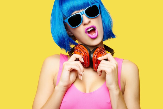 Girl dj in wig sunglasses and pink bathing suit listening music in headphones on yellow background. High quality photo