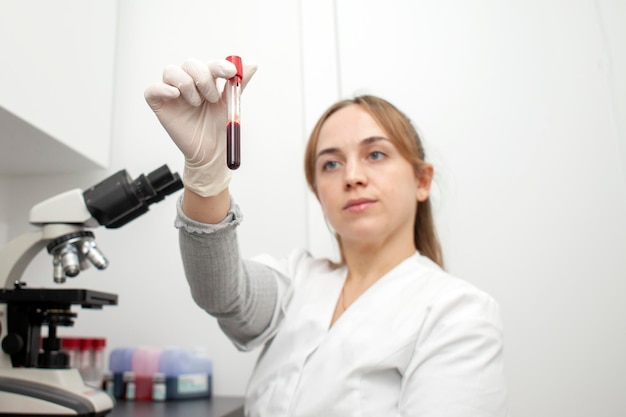 Girl doctor in the laboratory holds test tube with blood tests and looks at him woman nurse at work