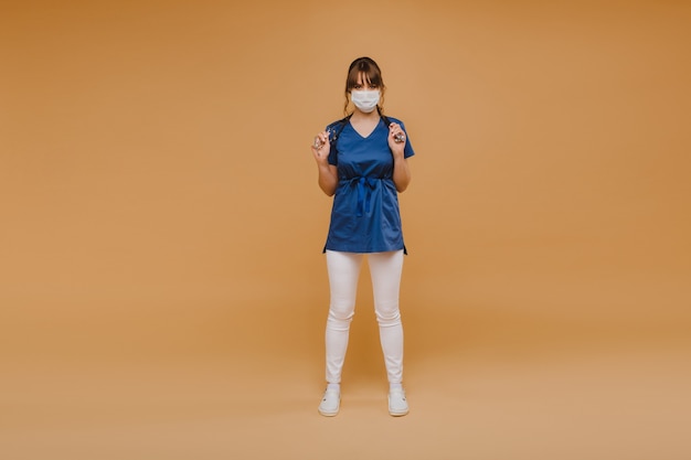 A girl doctor stands in a medical mask, isolated on a gray background.