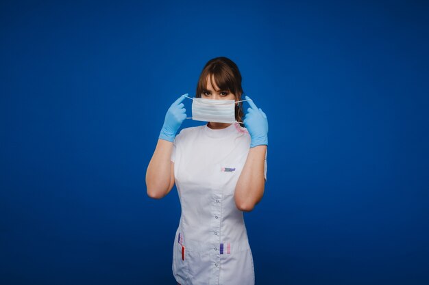 여자 의사는 회색 배경에 격리된 의료용 마스크를 쓰고 있습니다.