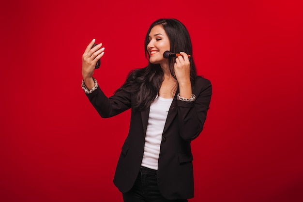 Girl does her makeup looking in a mirror on a red background