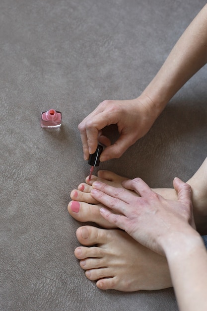 Girl does pedicure at home, vertical orientation. Female hands paint toenails with pink nail polish, close-up
