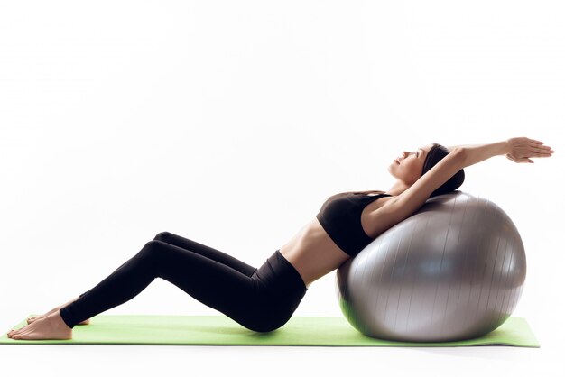 The girl does stretching on the ball in the white room.