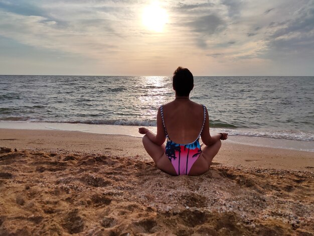 The girl does yoga exercises on the seashore A slender girl does gymnastics over the morning sun