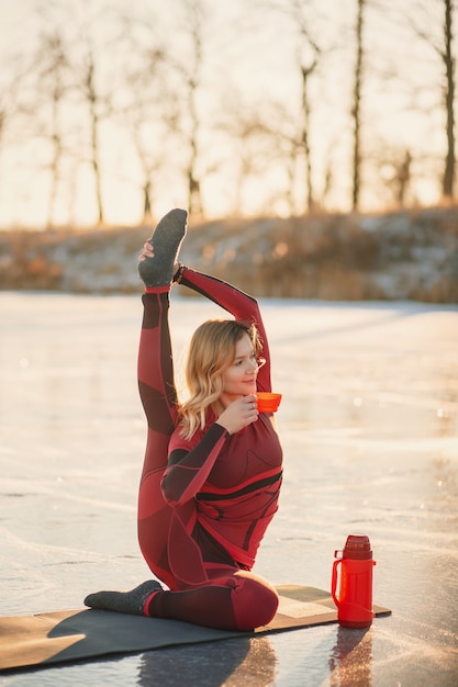 A girl does yoga in winter on the ice of the lake during the sunset