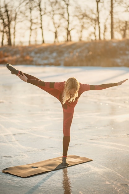 A girl does yoga in winter on the ice of the lake during the sunset