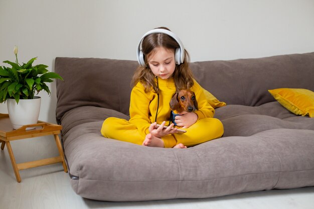 girl and dog are sitting on the bed and listening to music from a smartphone through headphones