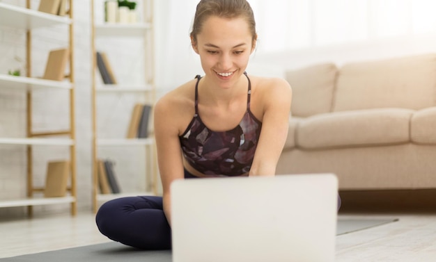 Foto ragazza che fa stretching a farfalla e guarda video tutorial online di yoga