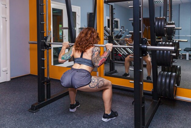 Girl doing exercises with a barbell girl with tattoos on fitness demonstrates a beautiful body
