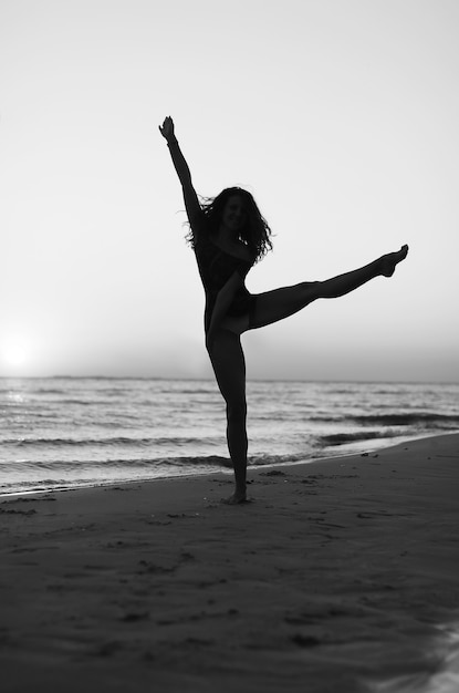 Девушка делает гимнастику на пляже на закате