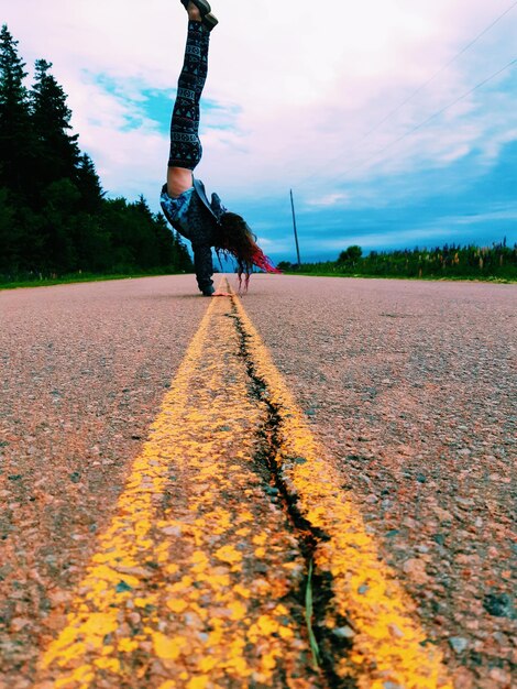 Girl doing handstand on road against sky