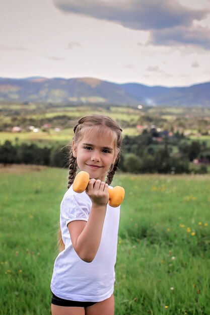 Girl doing her morning exercises with dumbbell on the top of the mountains in summer