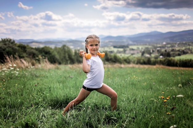 Girl doing her morning exercises with dumbbell on the top of the mountains in summer