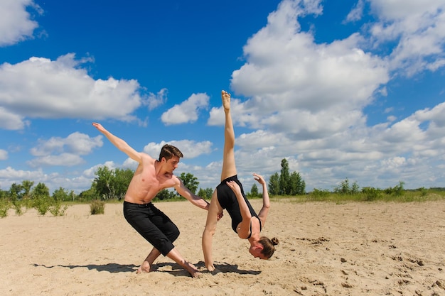 Girl doing splits against the sky clouds A man with naked torso on sand