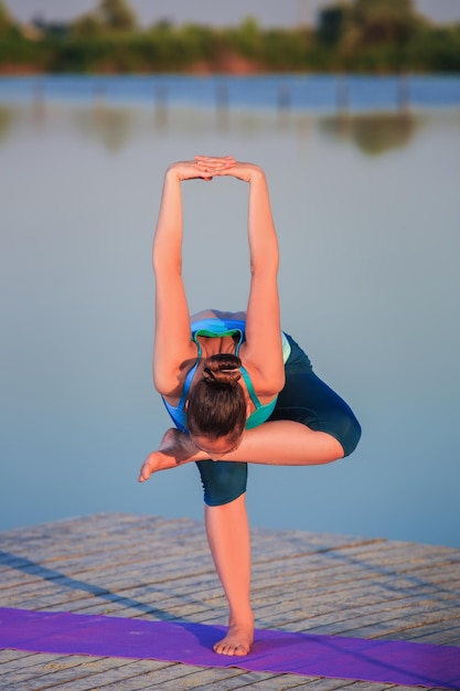 girl doing yoga exercises on the river bank at sunset