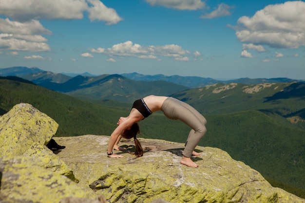 Девушка делает йогу на вершине горы.
