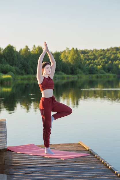 Girl doing yoga on wooden pier by lake in summer