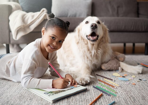Photo girl drawing and floor in portrait by dog coloring book or smile for learning education and development in home female child color pencil or art in notebook writing or pet on carpet in house