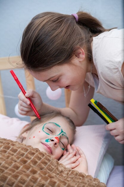 Girl drawing  mustache on  face of her sleeping sister . April Fool's Day