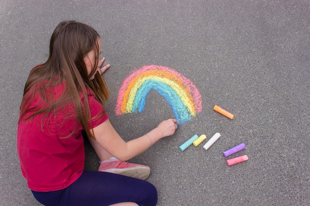 A girl draws a rainbow a house with chalk on the pavement