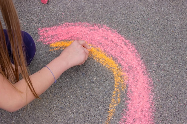 A girl draws a rainbow a house with chalk on the pavement