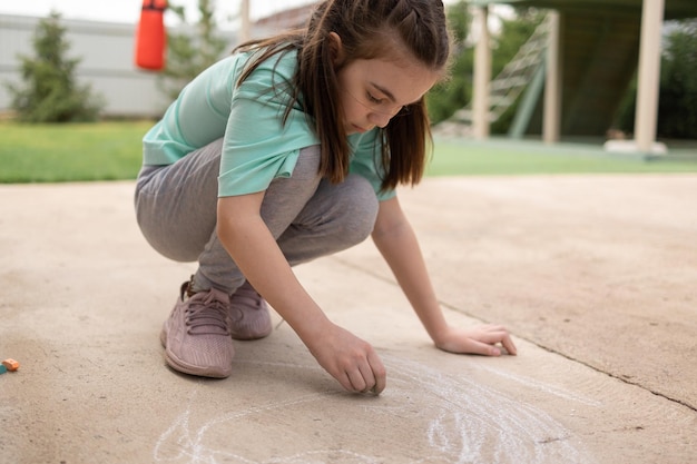 女の子は歩道にカラフルなクレイヨンで絵を描きます 子供の絵は壁にチョークで描きます 創造的な子供 子供の喜び